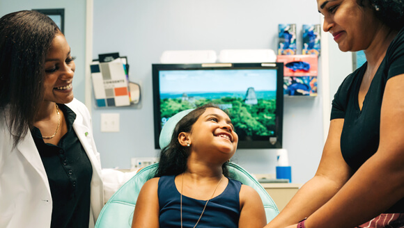 Child patient and mother smiling at each other as female dentist watches.