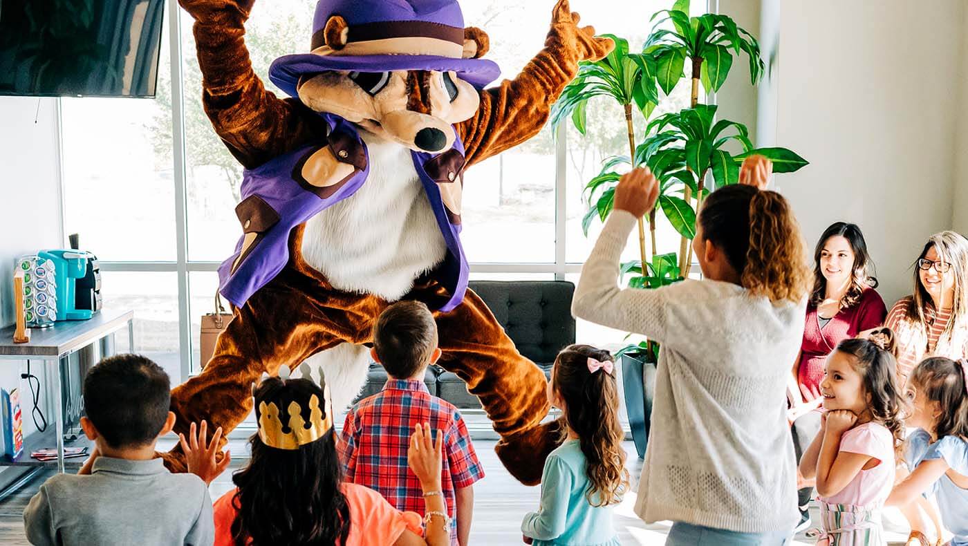 An office mascot jumps and plays with a group of pediatric patients, creating a positive dental office culture for patients.