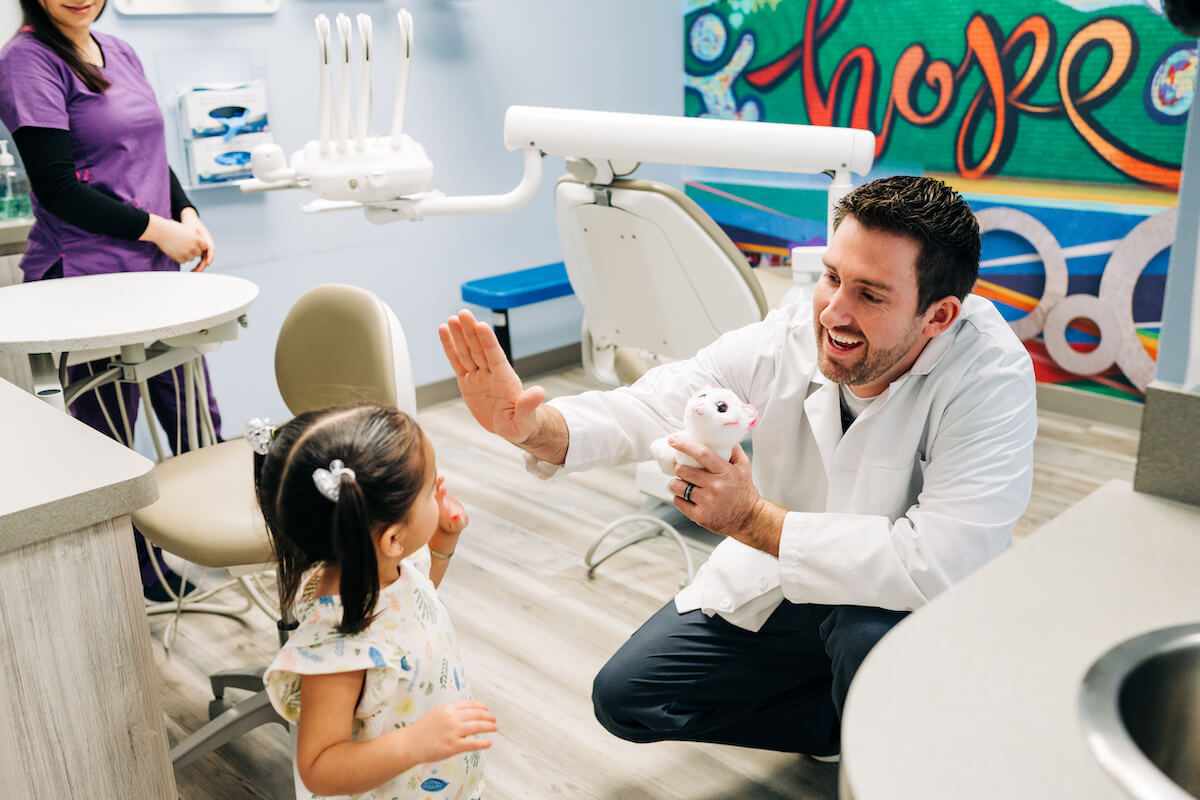 A CDP dentist kneels down to high-five a pediatric patient at one of their dental support organization-led practices.