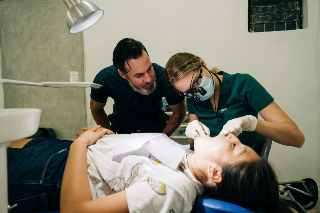 Dentist and dental assistant look inside a young female's mouth. Working with a great program and experienced mentor dentists is a must, especially if it’s your first time volunteering abroad.