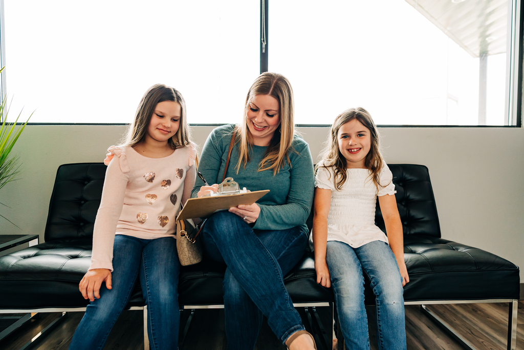Mother filling out patient paperwork with two daughters in the dentist office waiting room.